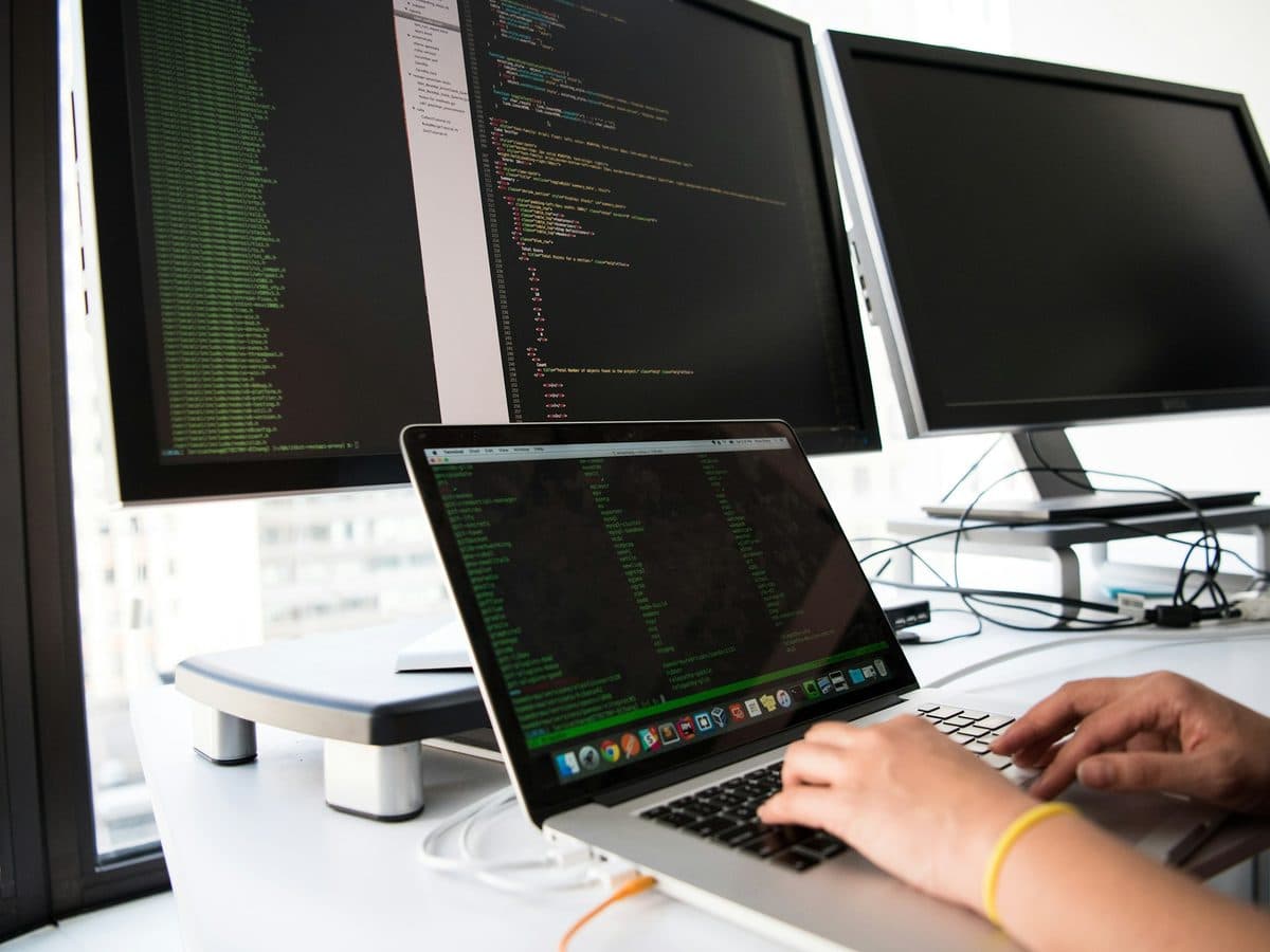 A developer working at a laptop and monitors showing code